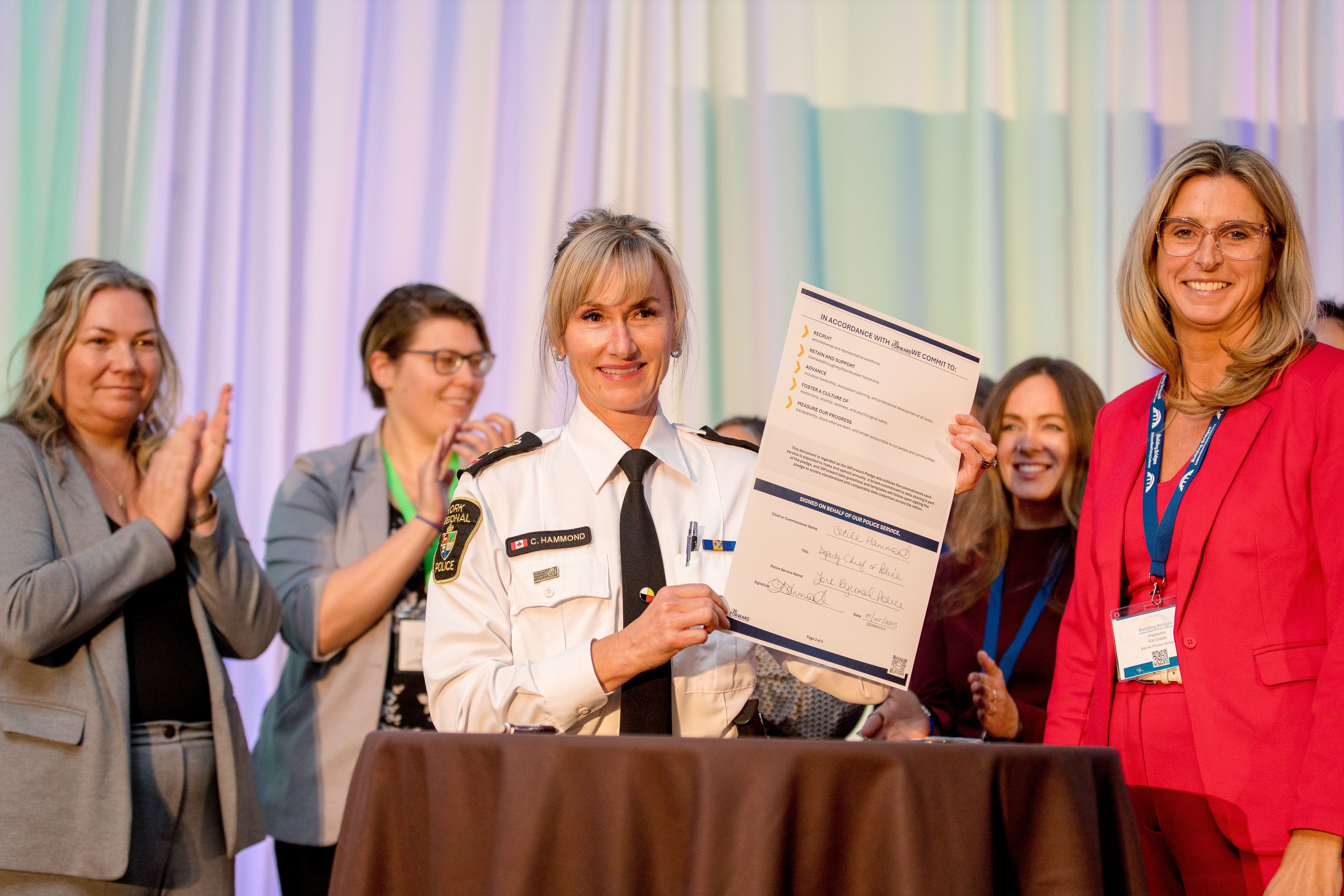 Deputy Chief Hammond signs 30Forward pledge Several women stand next to a police officer in uniform holding up a piece of paper