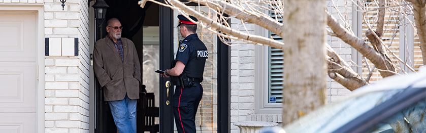 A man in a police uniform speaks to another man at the front door of a house