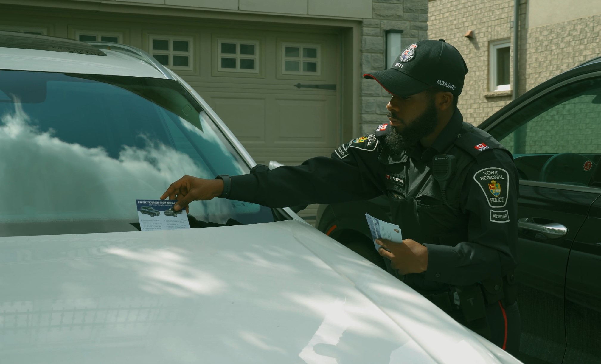 A man in a police uniform places a postcard on a car's windshield